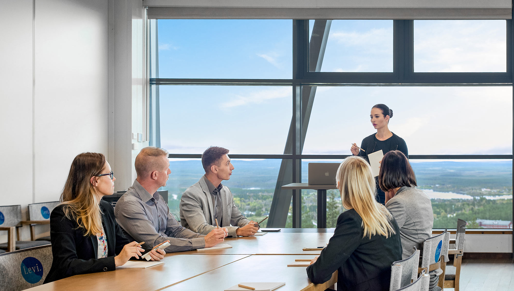 Ihmisiä kokouspöydän äärellä ja taustalla näkyvät upeat maisemat Levin kylän ylle.