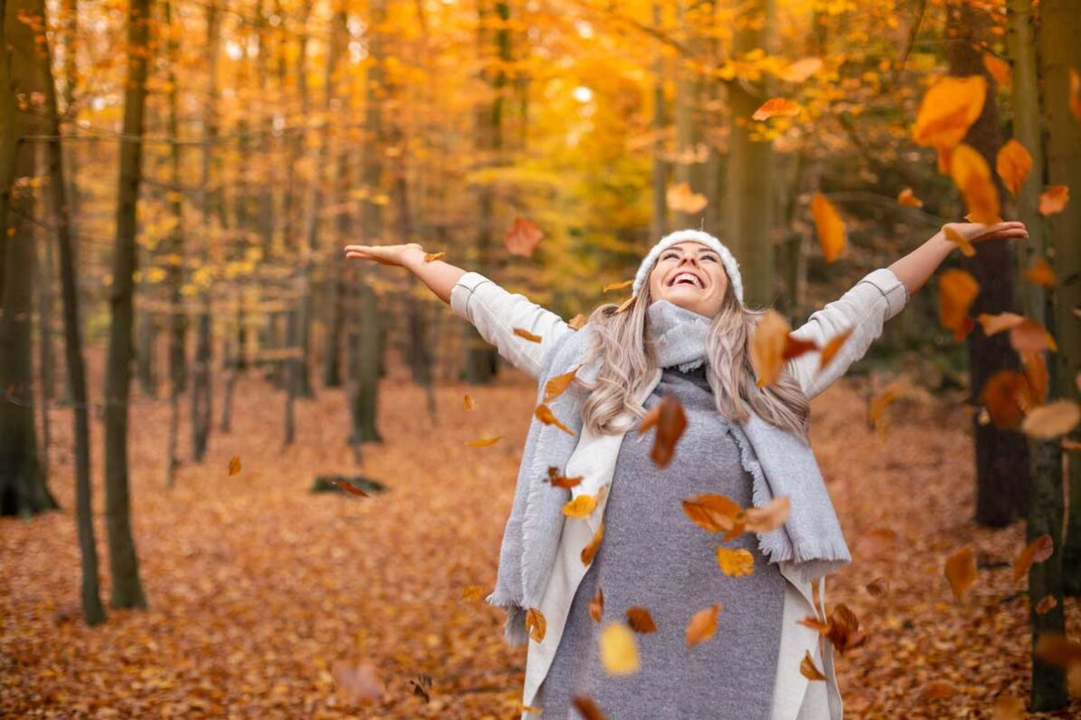 Nainen heittää maahan pudonneita lehtiä syksyllä.